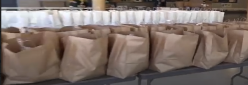 Shopping bags filled with food lined up on tables 